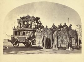 Photograph of the Maharajah of Alwar's state elephant carriage with at least three elephants (one hidden); many Europeans in the carriage and on the elephants. (Alwar)