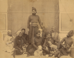 The Maharaja of Jaipur, H.H. Sir Sawai Madho II Singh, can be seen sporting a hunting costume, holding a rifle, accompanied by his entourage