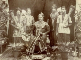 H.H. Umdae Rajhai Baland Makan Maharaja Shri Sir Sadul Singh Ji on his throne, attended by bearers carrying chauri and morchal