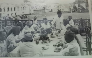 Photoghrap of Rewa cheifs taking breakfast in front of Rewah fort Palace where front view of fort palace has been capture with Maharaj saheb some car collection also be seen in Picture.